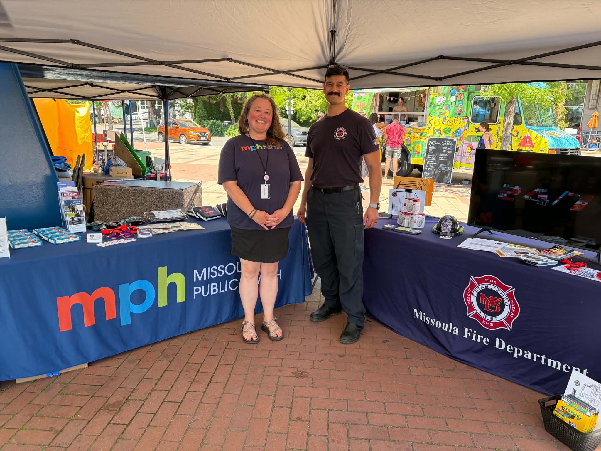 Two People standing in front of Missoula Public Health and Missoula Fire Department Tables in Caras Park