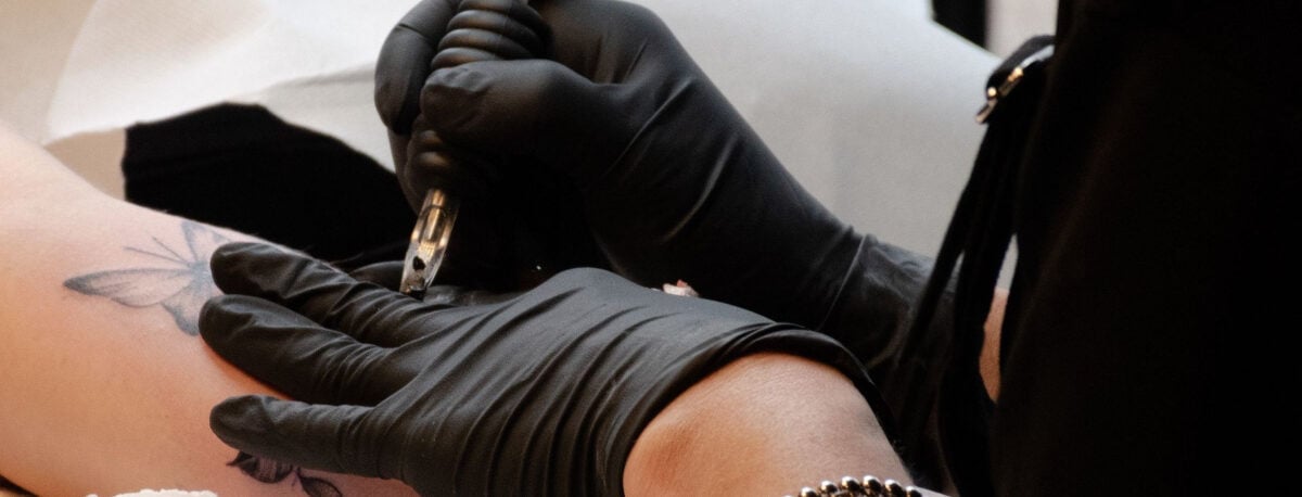 A tattoo artist wearing black gloves, giving a tattoo to a customer.