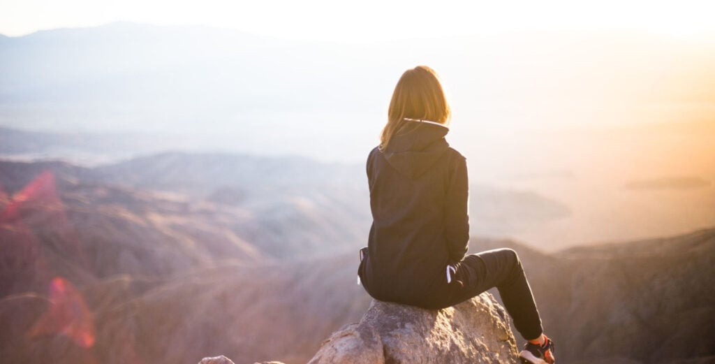 A woman sitting on top of a mountain and looking out at the view.