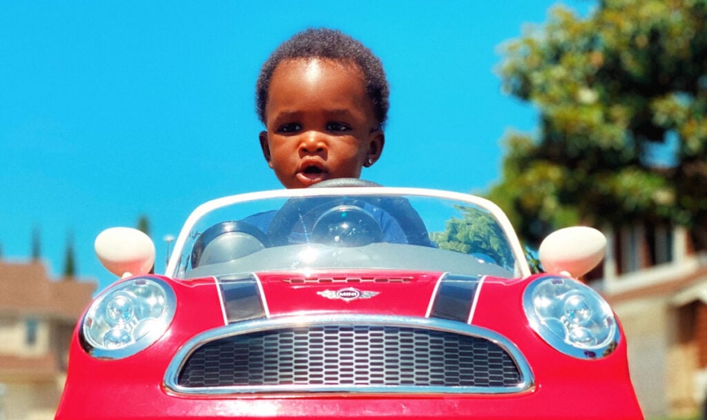 A toddler driving a toy car outside on a sunny day.