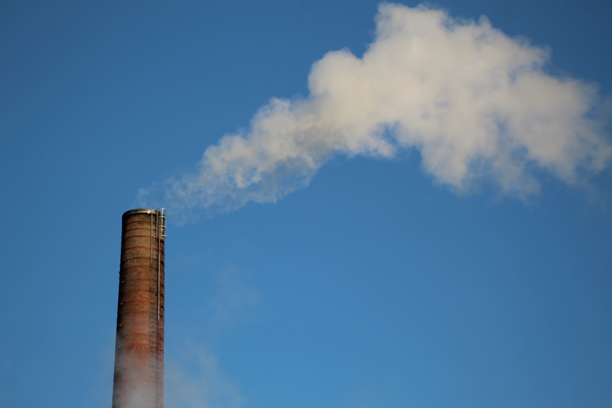 Grey smoke flowing out of a smoke stack in front of a blue sky.