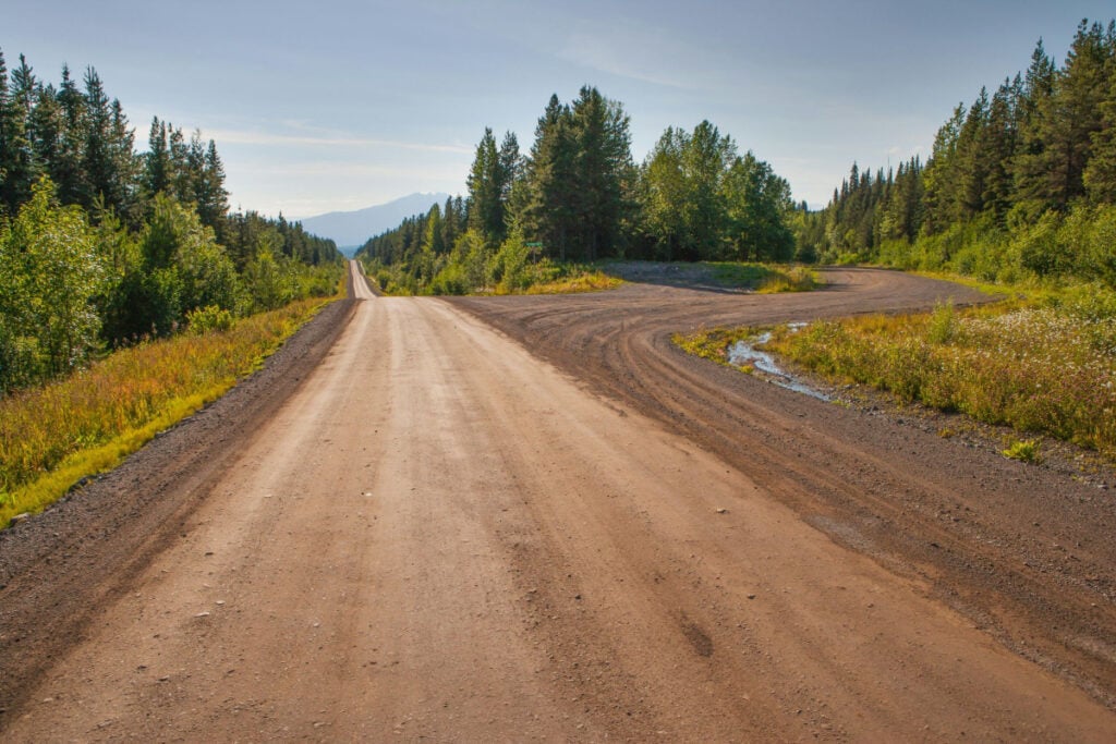 A dirt road surrounded by green trees.