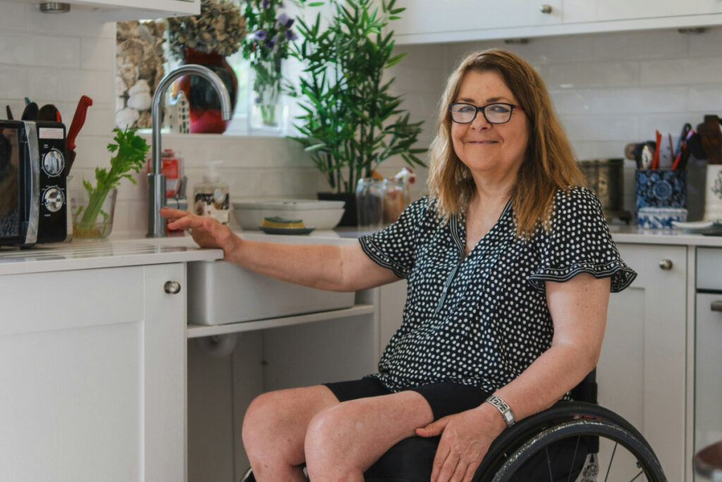 Women in wheelchair at sink in kitchen designed to be accessible to her.